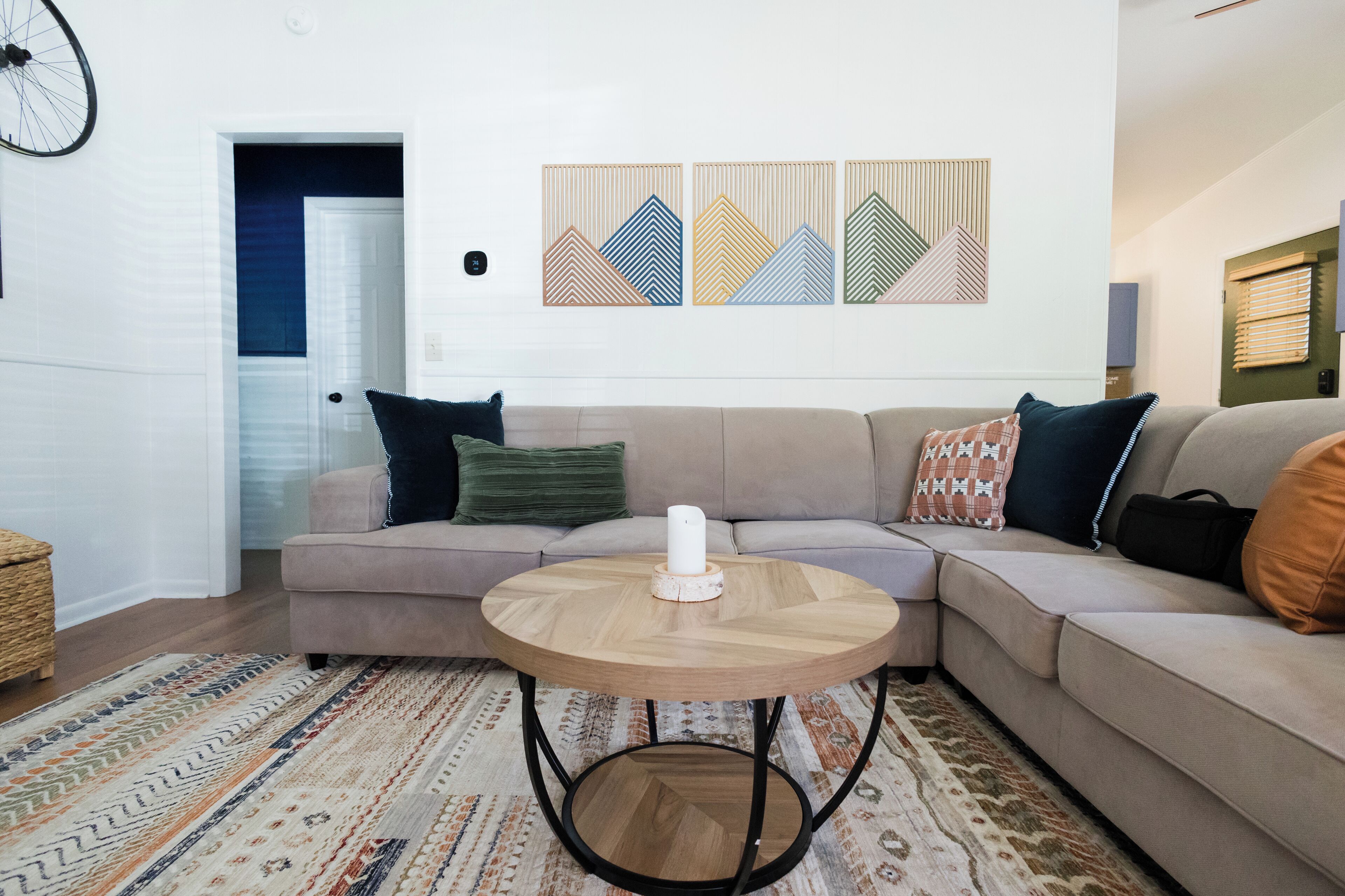 Una sala de estar con un sofá seccional color beige, una mesa redonda de madera y una alfombra estampada.