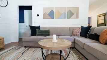 Una sala de estar con un sofá seccional color beige, una mesa redonda de madera y una alfombra estampada.