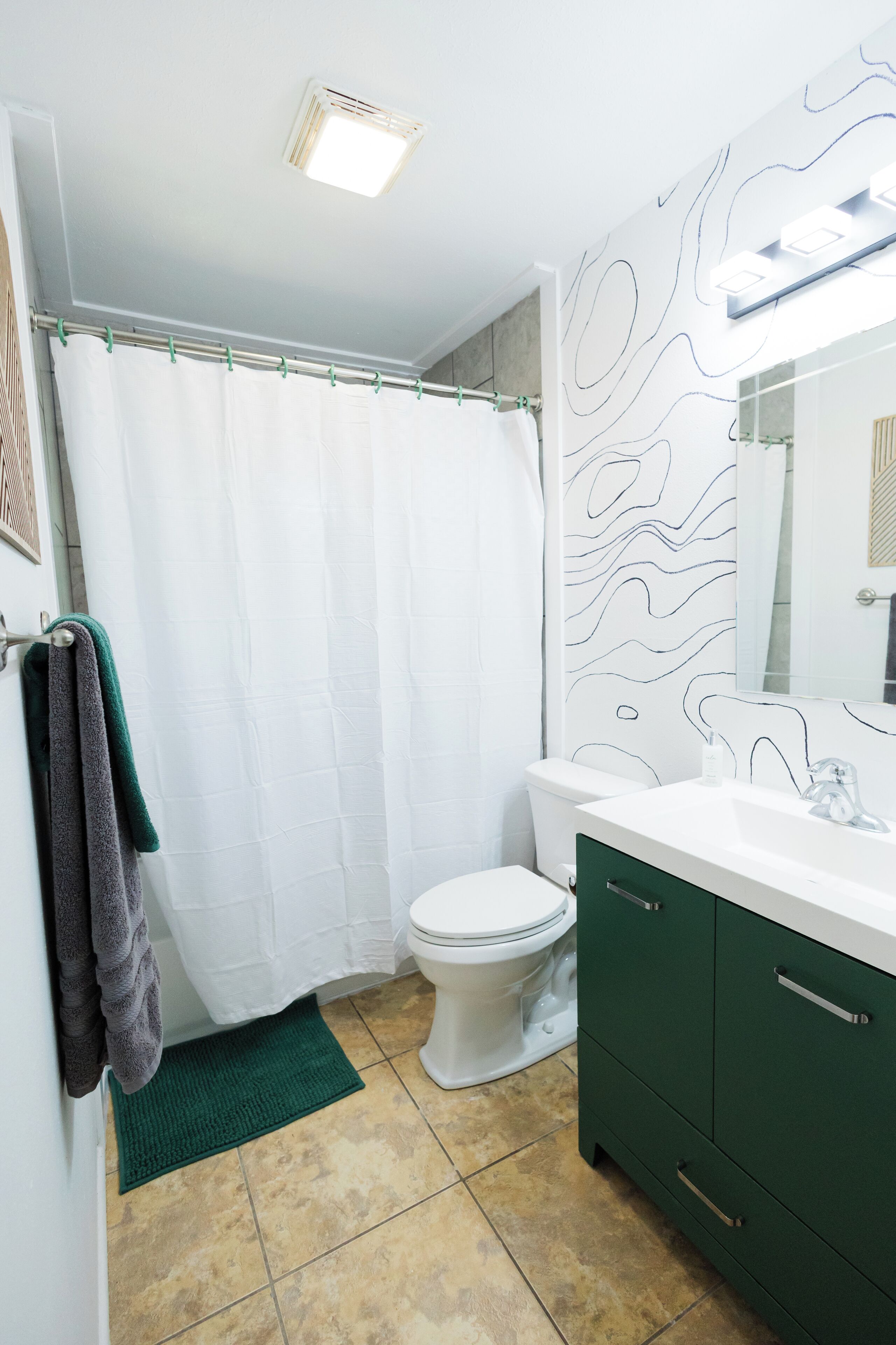 Un baño con inodoro blanco, armarios verdes, lavabo blanco y cortina de ducha.