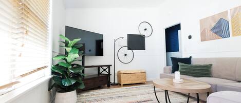 Ett modernt vardagsrum med en soffa, ett soffbord, en tv och en stor växt.