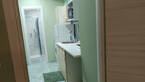 Un pasillo estrecho que da a una cocina con microondas, lavabo y cabina de ducha de vidrio.