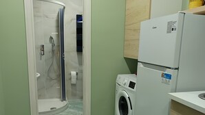 Un baño pequeño con ducha, lavadora y refrigerador.
