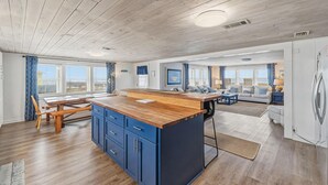Een ruime keuken met een houten eiland, blauwe kastjes en een eethoek met een tafel en stoelen.