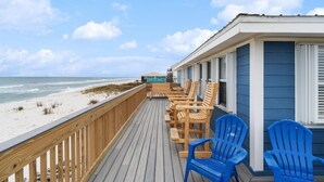 Een houten terras met blauwe stoelen met uitzicht op een strand.