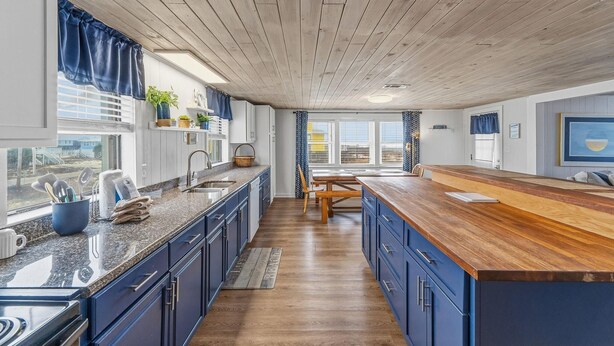 Een keuken met een houten plafond, blauwe kasten, granieten werkbladen en een houten eettafel.