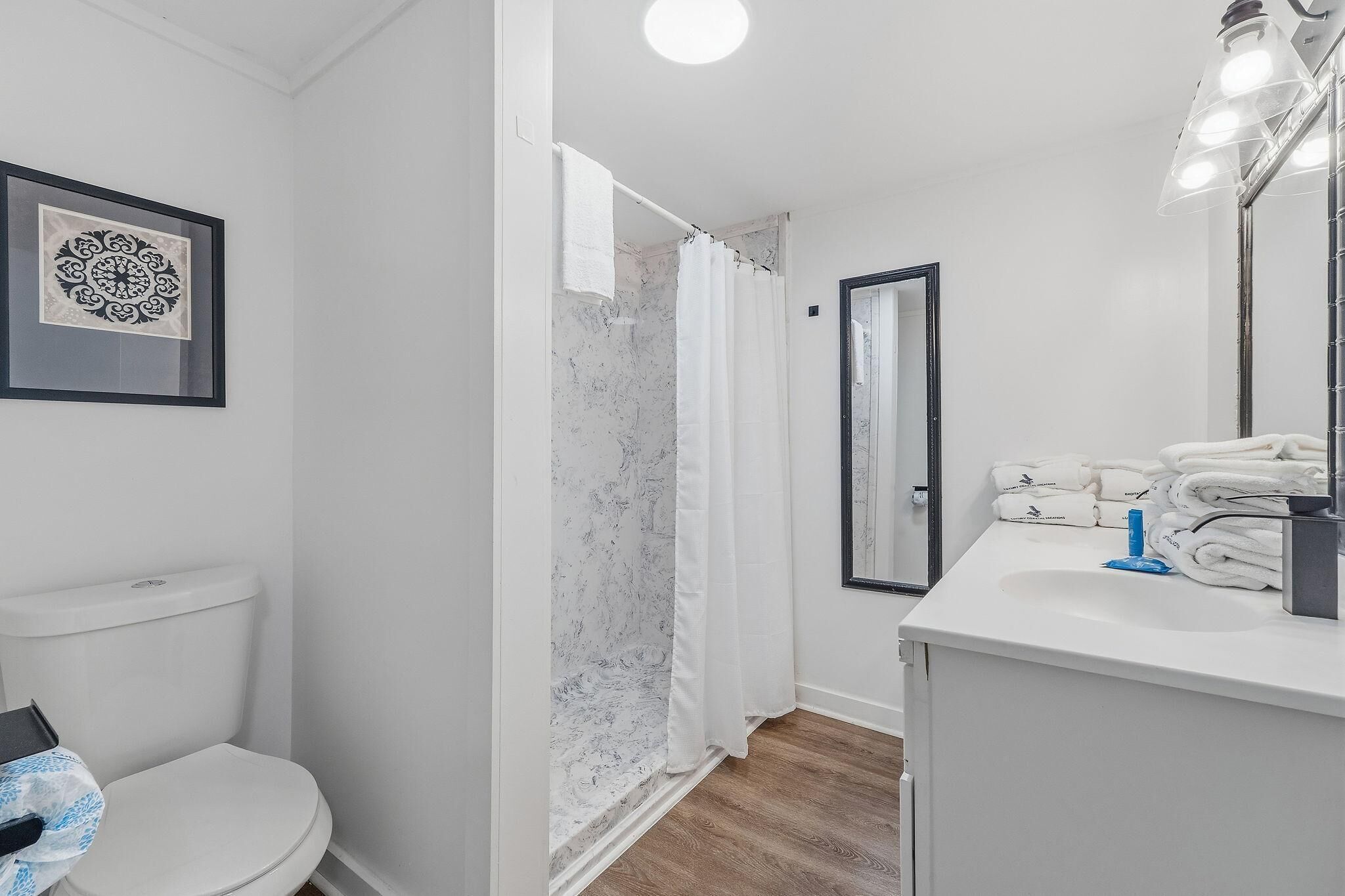 Ein Badezimmer mit Toilette, einer Dusche mit Marmorwand, einem Waschbecken mit Spiegel und einem gerahmten Kunstwerk an der Wand.