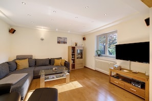 Una sala de estar moderna con sofá, mesa de centro, televisor, mueble de entretenimiento de madera y ventana con vistas.