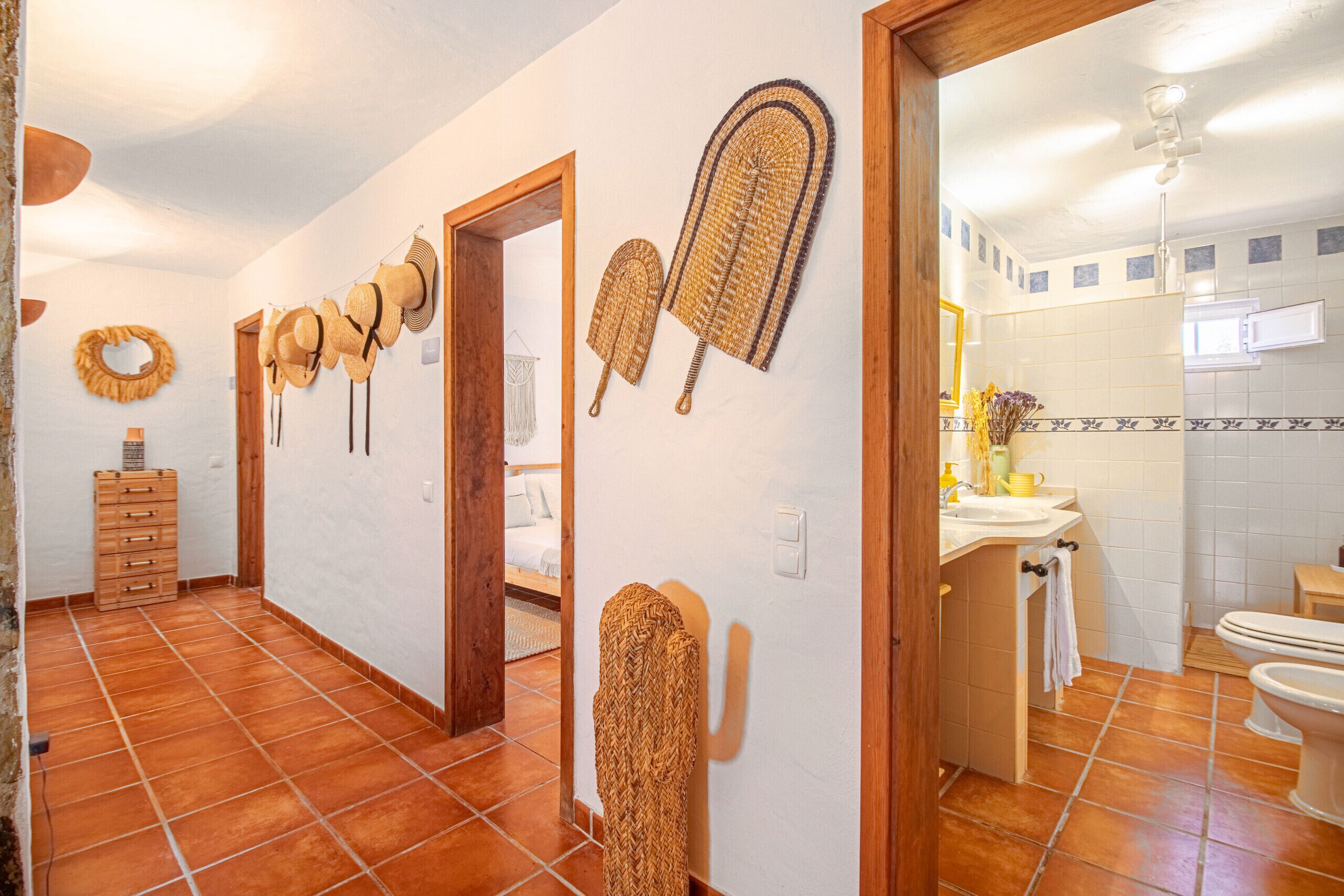 Un couloir avec une commode en bois, un miroir et un mur décoré de chapeaux tressés.