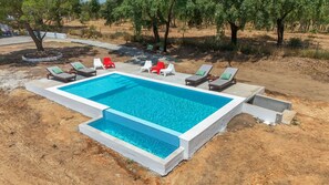Piscina retangular com borda branca, cercada por espreguiçadeiras e alguns vasos de plantas.