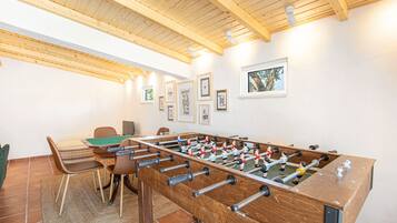 A room with a foosball table, wooden ceiling beams, and framed pictures on the wall.