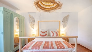 Quarto com cama, cabeceira de madeira, duas luminárias fixadas na parede e decoração na parede.