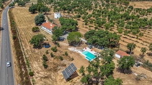 Vista aérea de uma propriedade com piscina, painéis solares e uma estrada próxima.