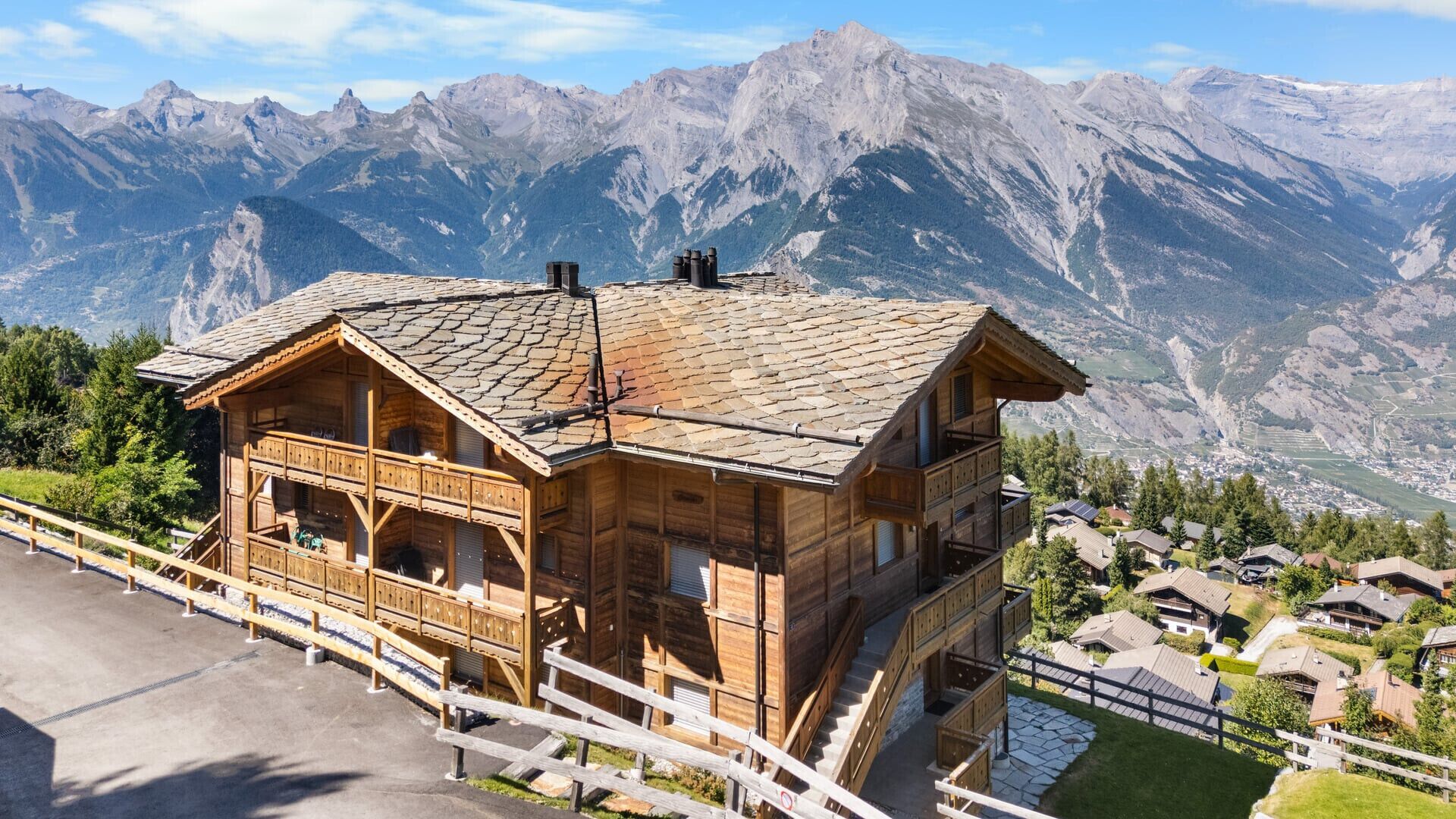A wooden chalet with a sloped roof, a balcony, and a view of mountains.