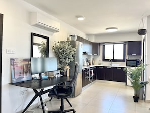 A modern kitchen with a dining area, a flat-screen TV, and a potted plant.