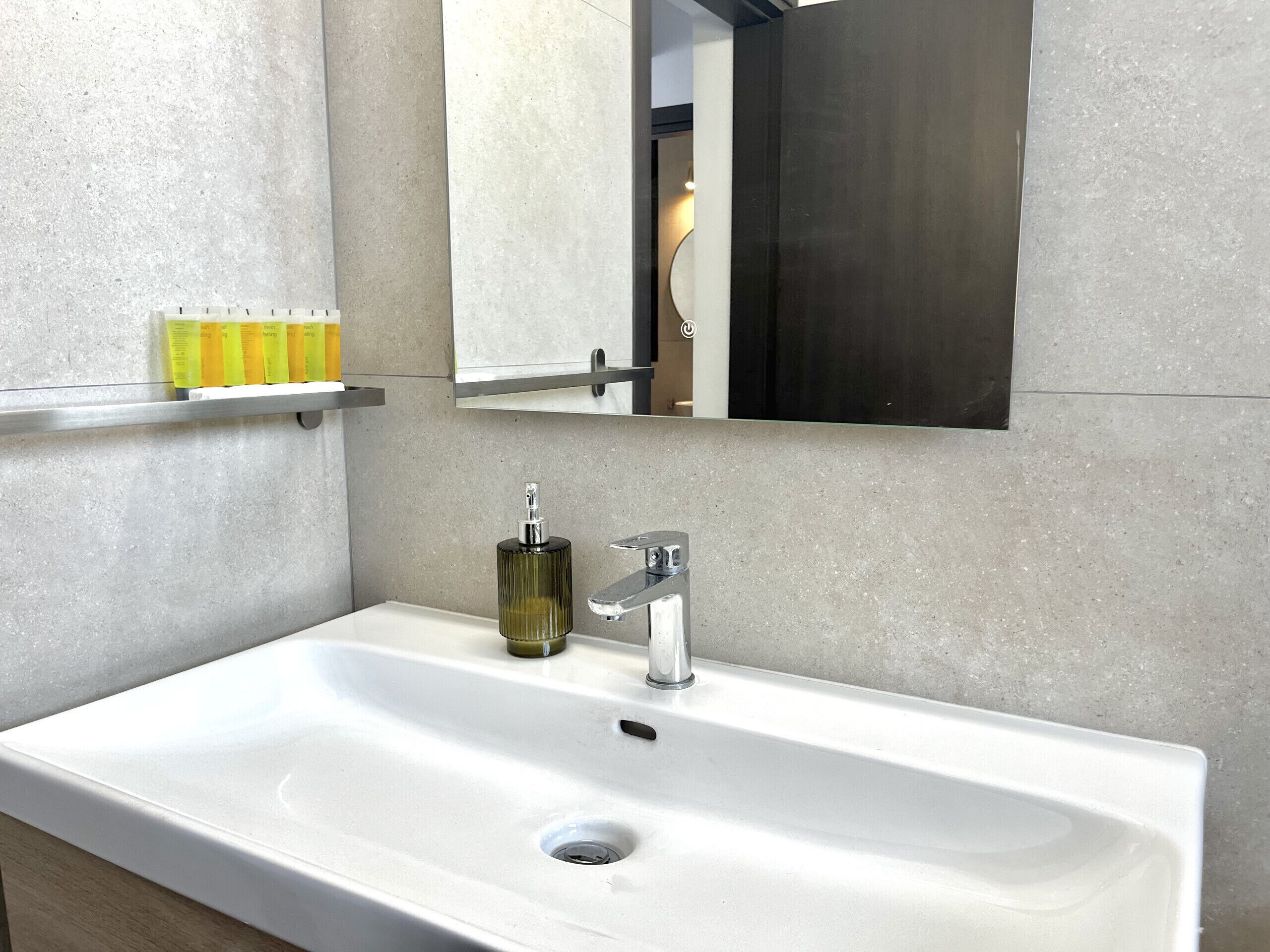 A modern bathroom with a white sink, a mirror above it, and a shelf with toiletries.