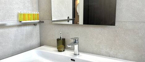 A modern bathroom with a white sink, a mirror above it, and a shelf with toiletries.