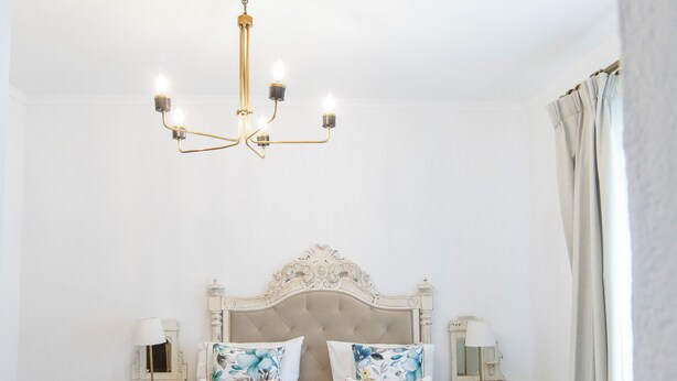 A neatly arranged bedroom with a large bed, two bedside tables, a chandelier, and a ceiling-mounted smoke detector. - Aposento Real Villas (Montemor-o-Novo)