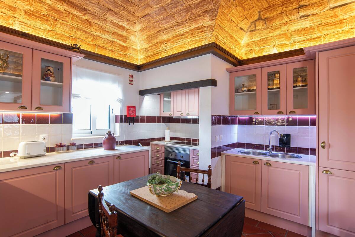 Una cocina con armarios rosados, techo de madera y una ventana.