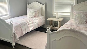 A bedroom with two white beds, a chandelier, and a window with blinds. - 3 bedroom walk to the beach! (Galveston)