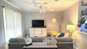 A living room with a sofa, a TV, a ceiling fan, and a table with decorative items. - 3 bedroom walk to the beach! (Galveston)