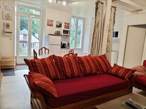 A cozy living room with a red sofa, wooden chairs, a small dining table, and a kitchen area with a refrigerator, microwave, and coffee maker. - Cosy apartment Ideal for hiking and nature (Laruns)