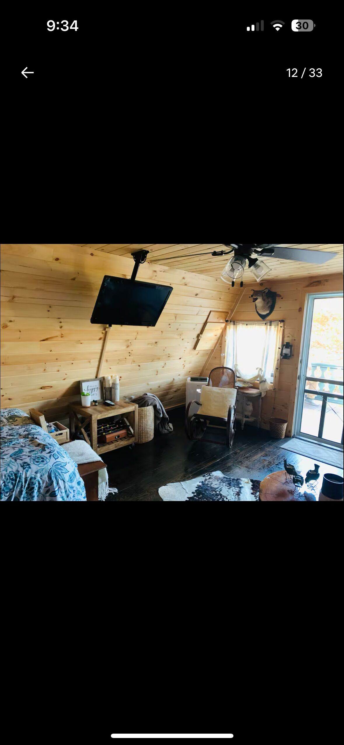 Ein gemütliches Blockhaus-Interieur mit Holzbalkendecke, einem an der Wand befestigten Fernseher, einem Rollstuhl und einem Fenster mit Blick ins Freie.