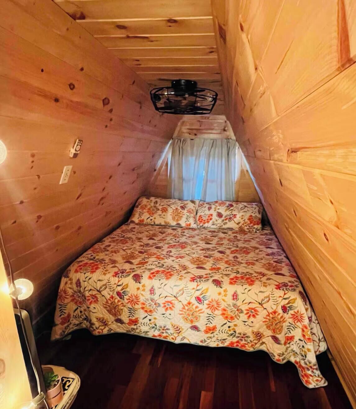 Een kleine, gezellige kamer met houten wanden en een bed met een bloemenprint.