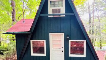 Eine kleine, dunkelblaue Holzhütte mit rotem Dach, umgeben von Bäumen.