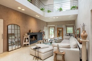 Ein geräumiges Wohnzimmer mit hoher Decke, Kamin, großzügigem Sofa und Balkon mit Pflanzen.