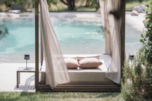 A bed with a canopy, positioned by a pool with a small table and lamp nearby.