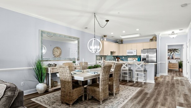Una cocina moderna con gabinetes blancos, electrodomésticos de acero inoxidable y un comedor con sillas de mimbre y una mesa blanca.