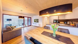 A modern living space with a wooden dining table, sofas, and a kitchen area with a TV and fruit bowl. - Urban-Apartmenthaus zwischen Berg und See (Dornbirn)