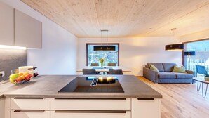 A modern kitchen with a central island, a dining area with a view, and a living space with a sofa and a balcony. - Urban-Apartmenthaus zwischen Berg und See (Dornbirn)