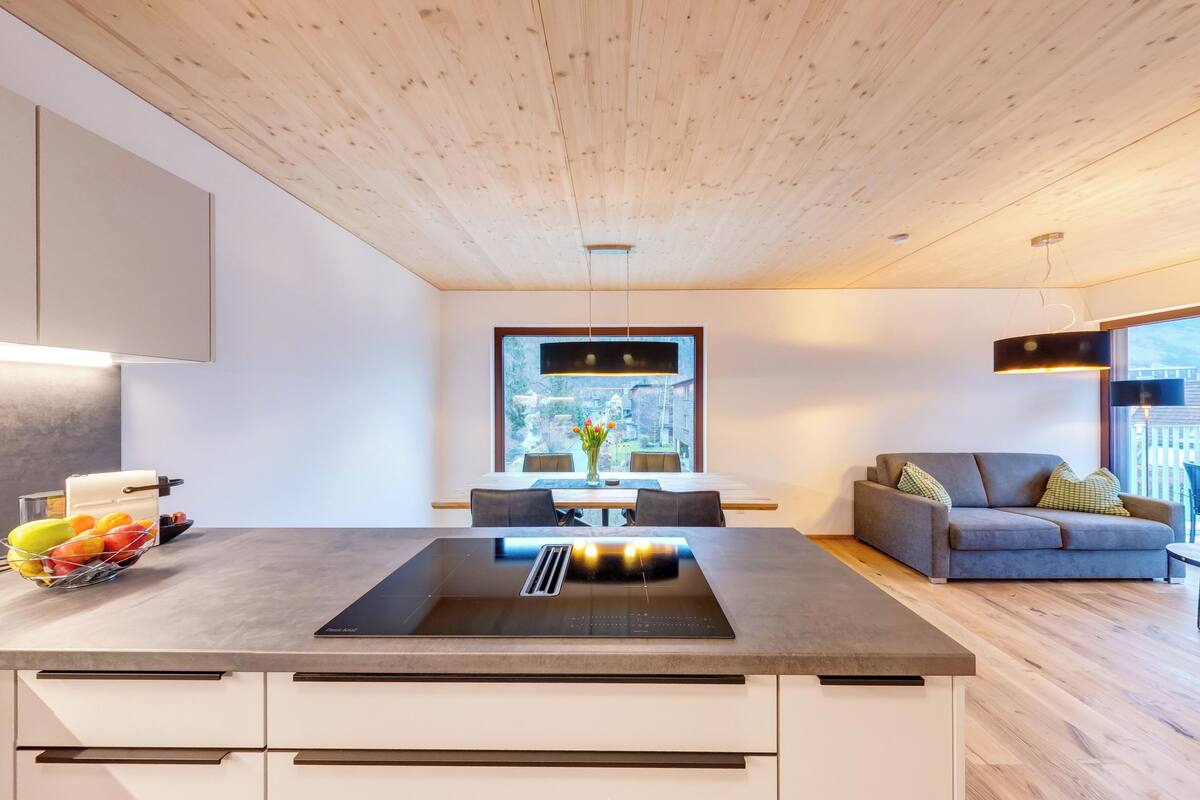 A modern kitchen with a central island, a dining area with a view, and a living space with a sofa and a balcony.
