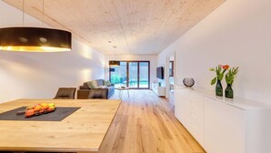 A modern living room with a wooden floor, a dining table with fruit, a sofa, and a TV. - Urban-Apartmenthaus zwischen Berg und See (Dornbirn)