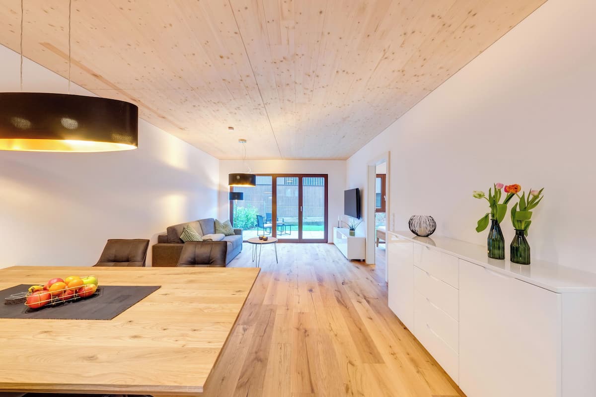 A modern living room with a wooden floor, a dining table with fruit, a sofa, and a TV.