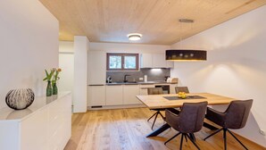 A modern kitchen with white cabinets, a wooden dining table, and a pendant light. - Urban-Apartmenthaus zwischen Berg und See (Dornbirn)