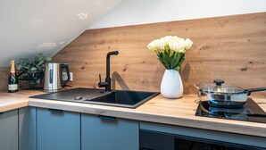 A modern kitchen with a wooden backsplash, a black sink, a stainless steel kettle, a white vase with flowers, and a stove. - RAW-Flats Milse - Modern. Stylish (Bielefeld)
