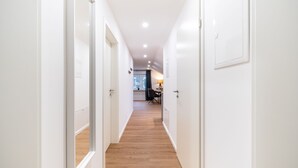 A narrow hallway with white walls and wooden flooring leading to a dining area with a table and chairs. - RAW-Flats Milse - Modern. Stylish (Bielefeld)
