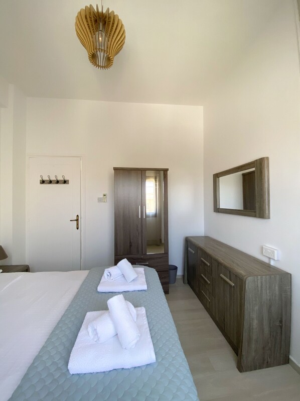 A hotel room with a bed, a dresser, a mirror, and a door with hooks.