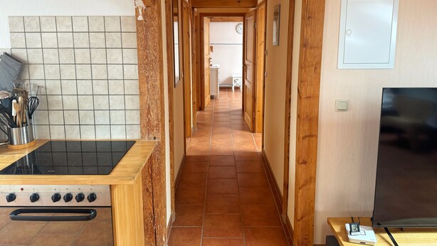 A kitchen with a stove, a sink, and a countertop with utensils. There is a hallway leading to a bedroom. - Charming top floor apartment near the Baltic Sea Ideal for families of up to 6 people (Rövershagen)