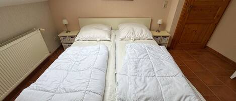 Una cama con dos plazas, ropa de cama blanca, una puerta de madera, un radiador y un cuadro en la pared.