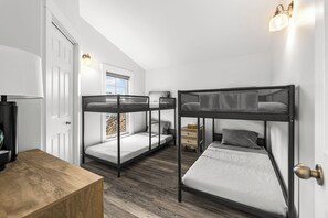 A room with bunk beds, a wooden desk, a lamp, and a dresser. - Premium Oceanfront Cottage Near Shediac | Modern Comforts & Stunning Views (Grande-Digue)