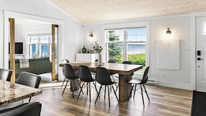 Une cuisine moderne avec une table et des chaises en bois, de grandes fenêtres donnant sur la mer et un canapé vert en arrière-plan.