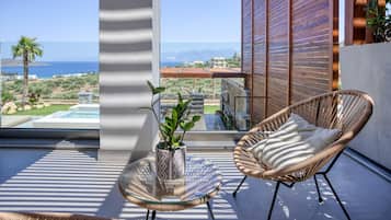 Un balcon avec un fauteuil en osier, une table en verre et un pot de fleurs.