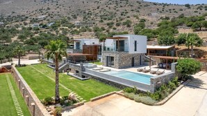A modern villa with a swimming pool, stone architecture, and a view of a hilly landscape.