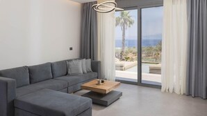 A modern living room with a grey sectional sofa, a wooden coffee table, and a large sliding glass door leading to a balcony with a view of palm trees and the sea.
