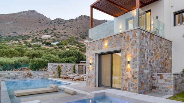 A modern house with a swimming pool, stone walls, and a view of a hilly landscape.