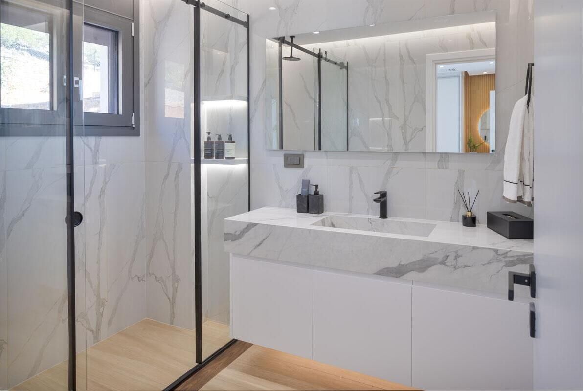 Une salle de bain moderne avec une douche à parois de verre, un grand miroir et un plan de toilette en marbre.