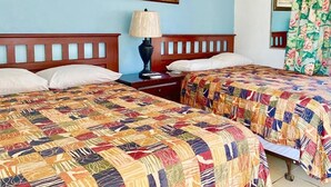 A hotel room with two beds, each with a colorful quilt, a nightstand with a lamp, and a painting on the wall. - Glades Motel (Naples)